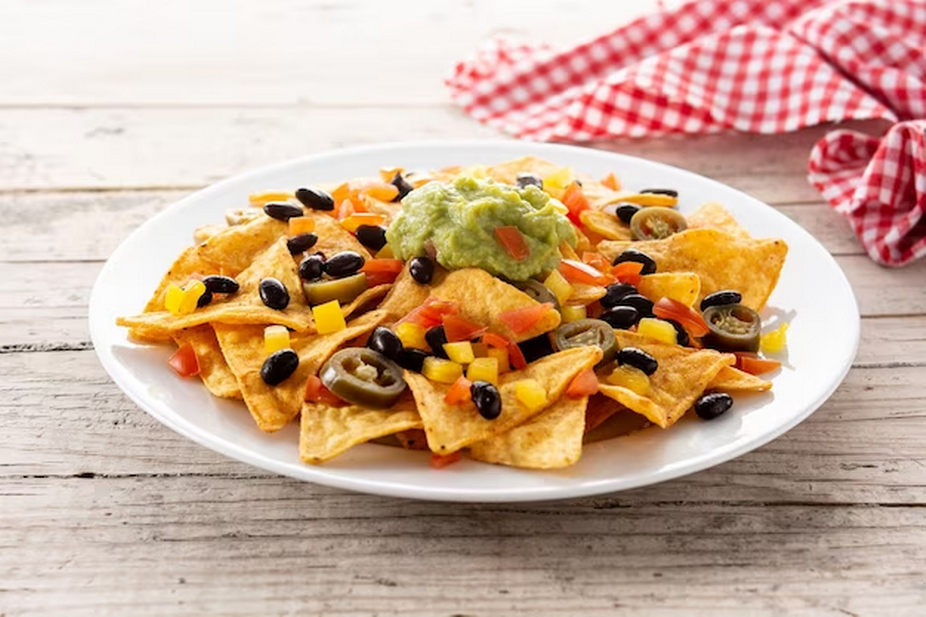 nachos tortilla chips with black beans, guacamole, tomato and jalapeno on wooden table